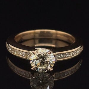 Gold engagement ring with a round center diamond and pavé diamonds along the band, photographed on a dark surface.