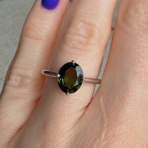 Close-up of a silver ring with an oval dark-green gemstone on a finger with purple nail polish