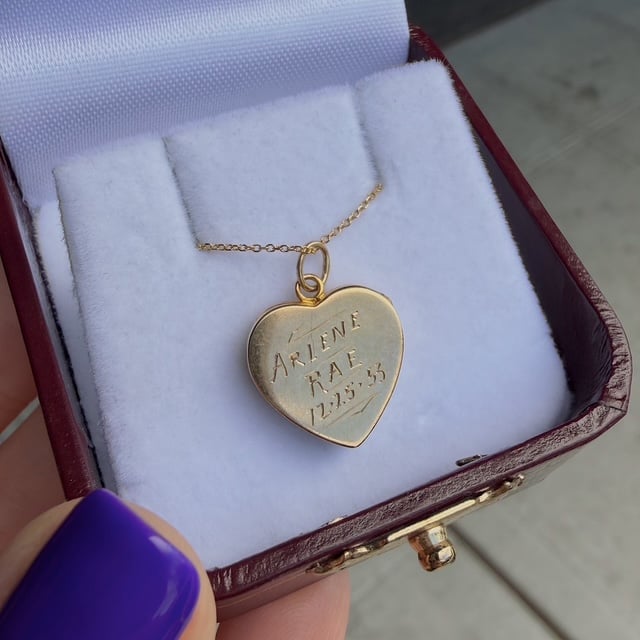 Gold heart-shaped pendant on a delicate chain, resting on white velvet padding inside a burgundy jewelry box.