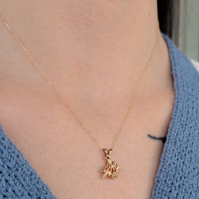 Close-up of a delicate gold necklace with a leaf‑flower cluster pendant resting on the neck.