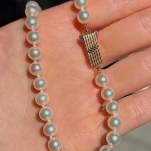 Pearl necklace with round white beads and a gold geometric clasp resting on a hand.