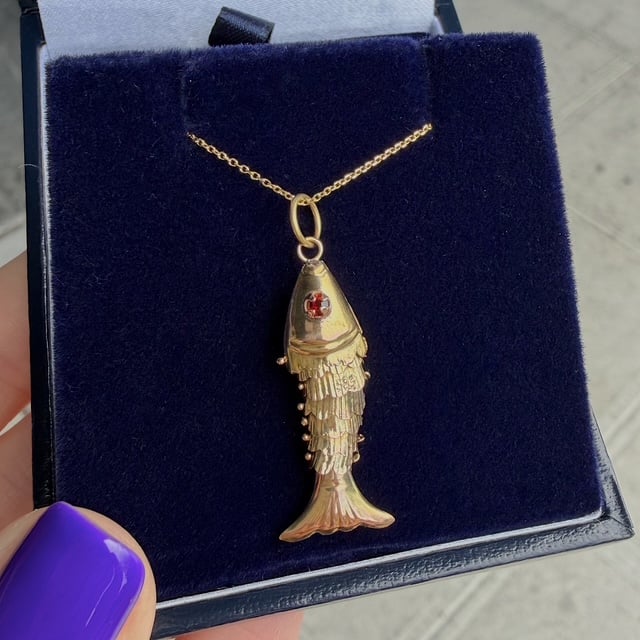 Gold fish pendant necklace with a red gem eye on a blue velvet jewelry display box.