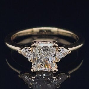 Diamond engagement ring with a rectangular emerald-cut center stone and two side diamonds on a gold band.