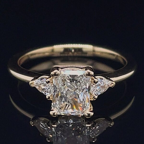 Diamond engagement ring with a rectangular emerald-cut center stone and two side diamonds on a gold band.