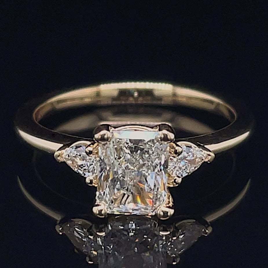 Diamond engagement ring with a rectangular emerald-cut center stone and two side diamonds on a gold band.