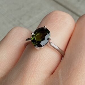 Oval dark-green gemstone ring on a finger with a silver band and four-prong setting (close-up)