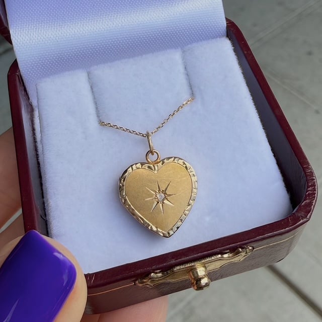 Gold heart pendant with a starburst gem, on a delicate chain inside a blue velvet-lined jewelry box.