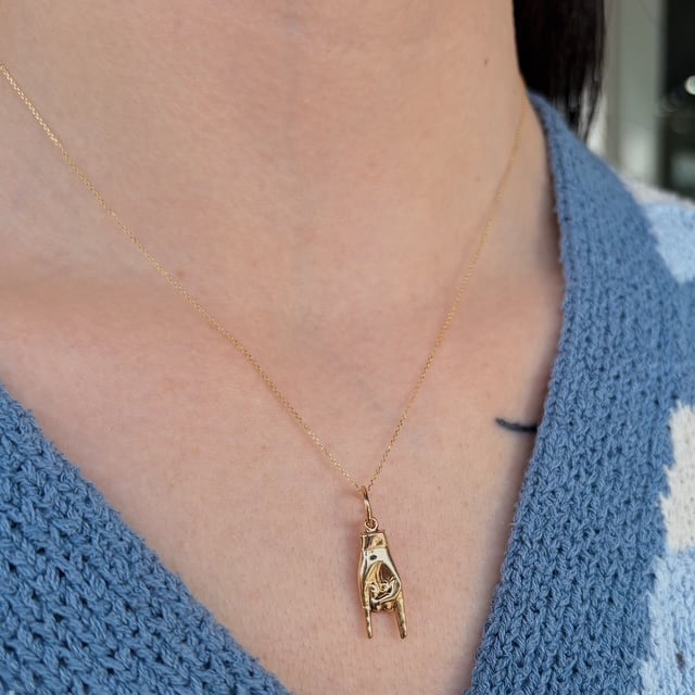 Gold chain necklace with a small rectangular pendant containing a tiny carved figure, resting on a blue knitted top.