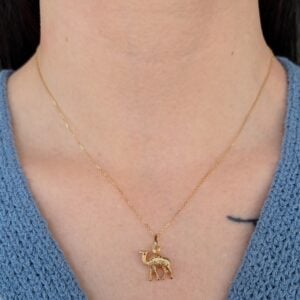 Gold necklace with a small camel pendant resting on a light neck over a blue knit top.