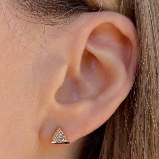 Close-up of a left ear wearing a gold triangle-shaped diamond-studded stud earring.