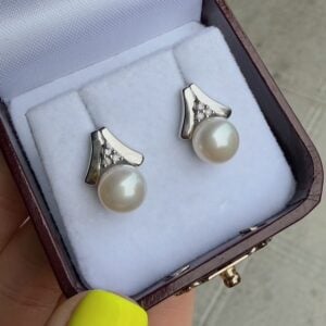 Pearl stud earrings with silver settings and crystal accents in a white cushioned jewelry box.