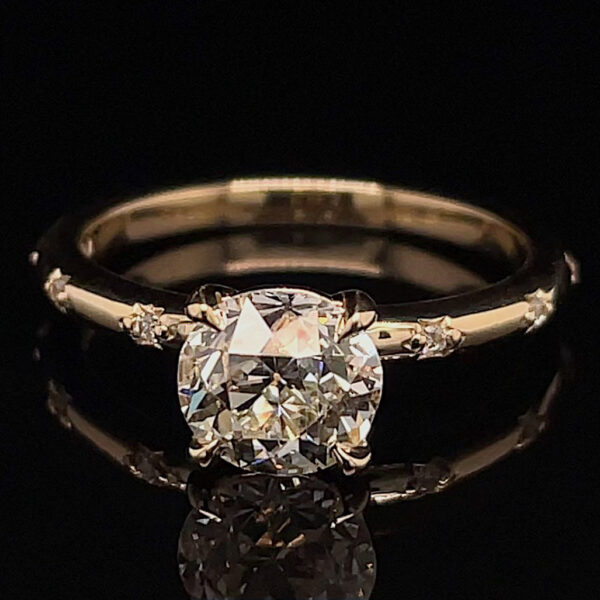 Gold band engagement ring with a large round-cut diamond and small side stones, photographed against a black background, showing sparkle and reflections.