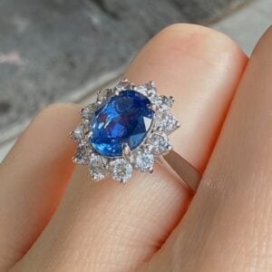 Blue gemstone ring with halo of diamonds on a silver band worn on a finger, close-up detail.
