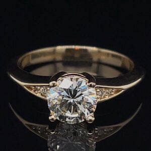 Engagement ring with a large round-cut diamond solitaire and small side diamonds on a gold band against a dark background.