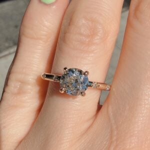 Rose gold engagement ring with a large round-cut diamond and small diamonds along the band on a finger.