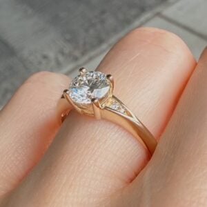 Gold ring with a large round diamond held by four prongs on a finger, close-up view.