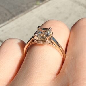Rose gold engagement ring with a rectangular-cut diamond on a finger, highlighted by sunlight.