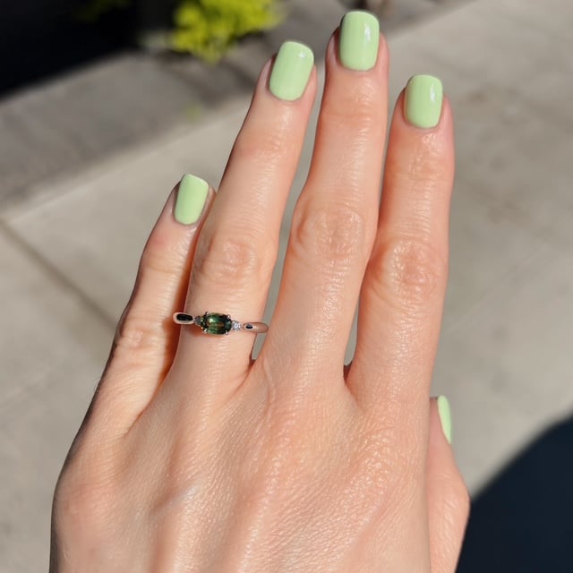 Hand with mint green manicured nails wearing a silver ring featuring a green oval gemstone flanked by small stones on a thin band.