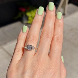 Close-up of a hand with mint-green manicured nails wearing a gold ring with a rectangular blue gemstone and small surrounding stones.