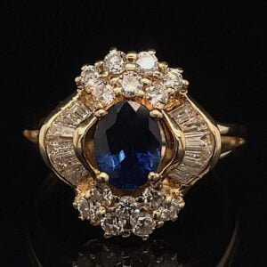Gold ring with an oval blue sapphire center surrounded by a halo of diamonds on a dark background.