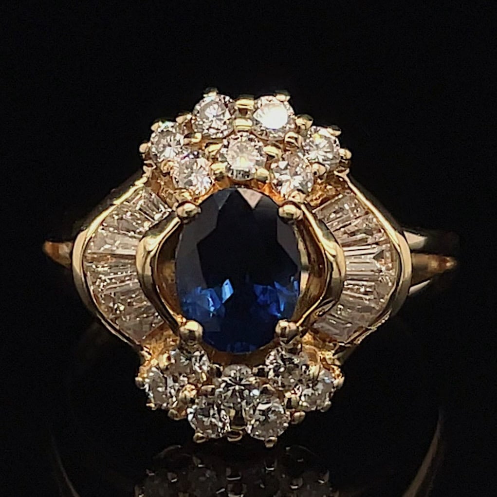 Gold ring with an oval blue sapphire center surrounded by a halo of diamonds on a dark background.