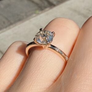 Close-up of a diamond solitaire ring on a finger, set in rose gold with sunlight sparkling the stone.