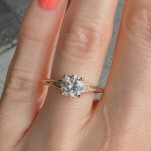 Rose gold solitaire engagement ring with a large round diamond on a finger, close-up shot.