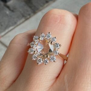Flower-shaped halo ring: peach center stone surrounded by diamond petals, worn on finger.