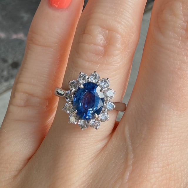 Oval blue sapphire ring with a halo of diamonds, shown on a finger.