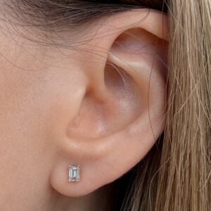 Emerald-cut diamond stud earring on a person's earlobe with light hair nearby lush skin tone detail