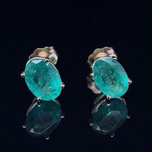 Oval teal gemstone stud earrings in a silver prong setting on a black mirrored surface