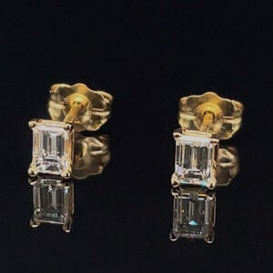 Two gold earrings each with two emerald-cut diamonds stacked vertically, set in prong settings on a dark background.