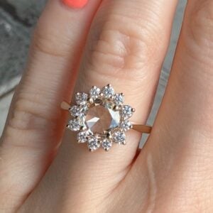 Gold ring with a large central gemstone surrounded by a halo of diamonds on a finger.