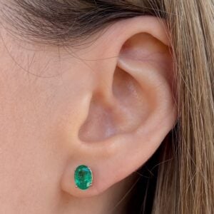 Emerald green oval gemstone stud earring on the earlobe with silver prongs.
