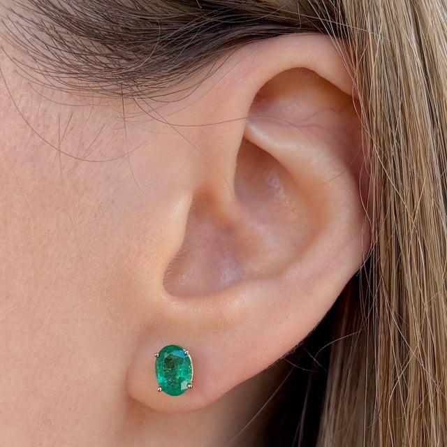 Emerald green oval gemstone stud earring on the earlobe with silver prongs.