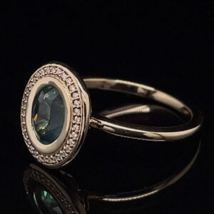 Engagement-style ring with an emerald-green center stone surrounded by a halo of small diamonds on a silver band on a dark background.