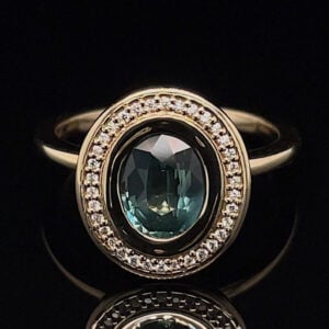 Gold ring with an oval teal center stone, surrounded by a halo of small diamonds on a black background.