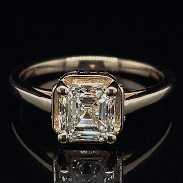 Emerald-cut diamond ring with a four-prong setting on a sleek metal band, photographed against black background.