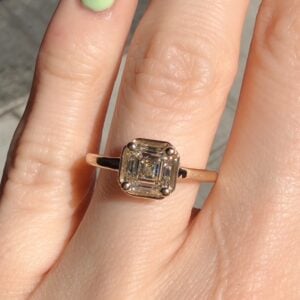 Gold ring with an emerald-cut diamond on a finger, four-prong setting