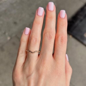 Close-up of a hand with pale pink manicured nails and a wavy gold ring on the ring finger.