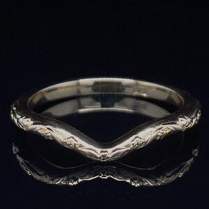Silver ring with an engraved floral vine pattern along the band, forming a subtle V in the center against a black background.