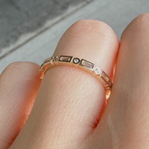 Rose gold ring with alternating rectangular and round stones worn on a finger.