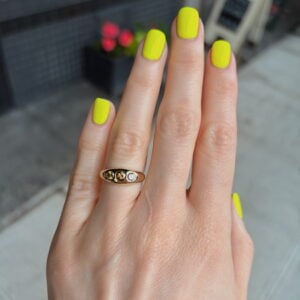 Close-up of a hand with neon yellow manicure and a gold ring with three stones on the ring finger,