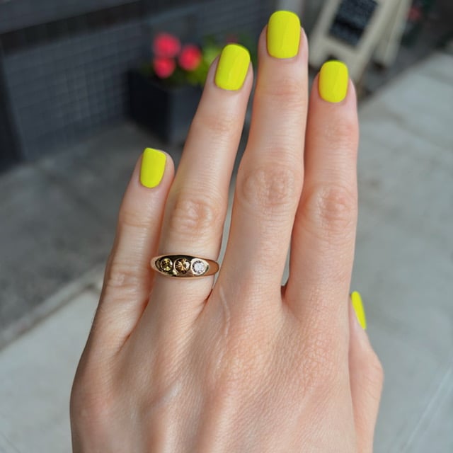 Close-up of a hand with neon yellow manicure and a gold ring with three stones on the ring finger,