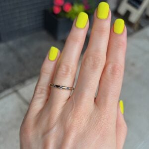 Hand with neon yellow manicure and a thin gold ring with blue stones on the ring finger.
