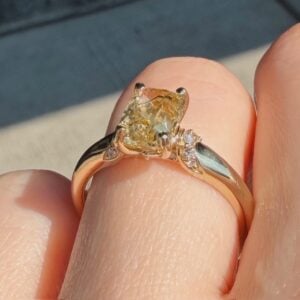 Rose gold engagement ring with a cushion-cut yellow center diamond and small diamonds on the shoulders, worn on a finger.