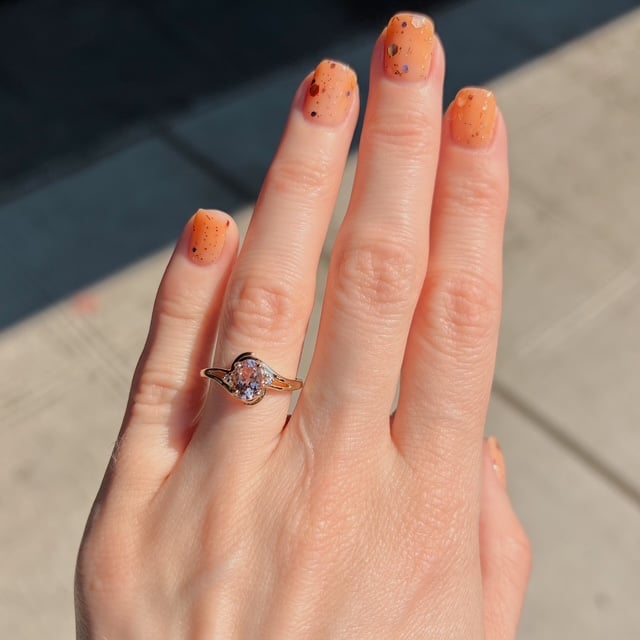 Close-up of a hand with orange speckled nail polish wearing a rose-gold ring with a round diamond on the ring finger.