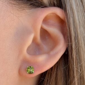 Green square-cut gemstone stud earring on the earlobe of a person,”