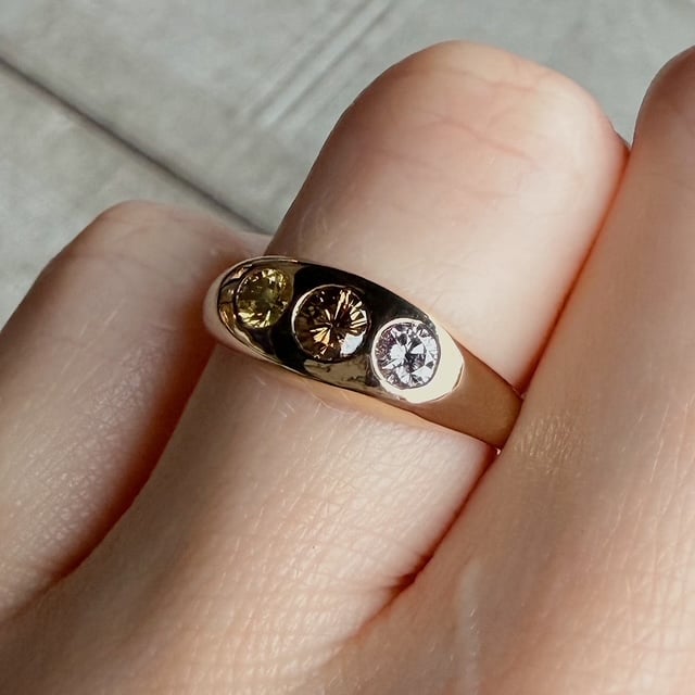Close-up of a gold band ring with three round gemstones (green-yellow, brown, and clear) on a finger