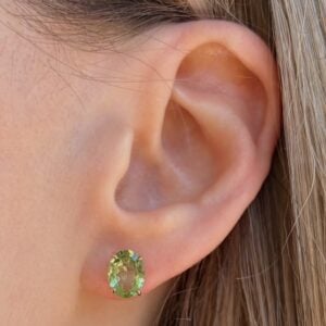 Close-up of a earlobe with a green oval gemstone stud earring in a gold setting